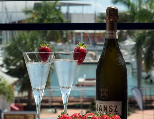 Two flutes of sparkling wine with strawberries next to an unopened bottle of Jansz sparkling wine